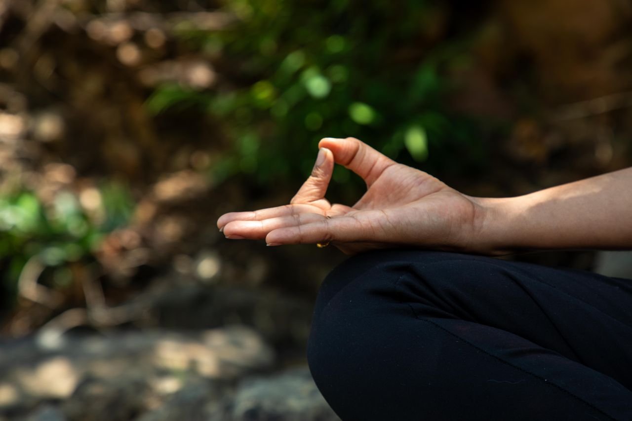 A close-up shot of a hand performing a meditation pose outdoors, surrounded by nature.