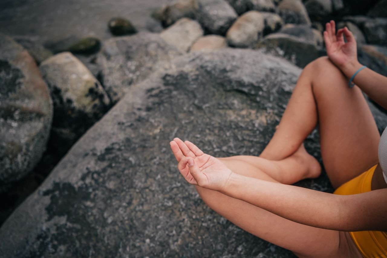 The Art of Drawing Readers In: Your attractive post title goes here A woman in a meditative pose on a seaside rock, focusing on mindfulness and relaxation.